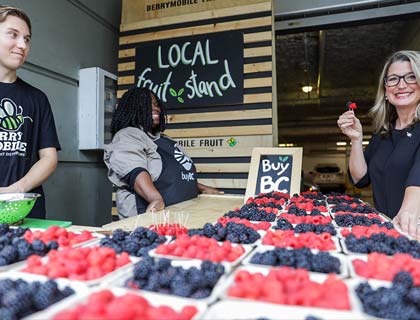 Woman holding a strawberry visiting a local fruit stand.