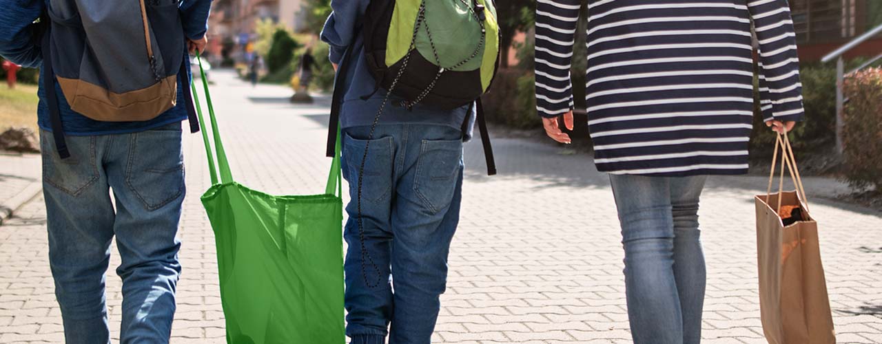Mother walking with two young boys holding reusable shopping bags.