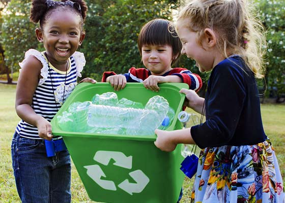 Three children holding a recycling container filled with plastic bottles.