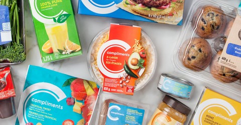 Two plates of grilled salmon with quinoa and orange slices on a white table with blue glasses, utensils, and a pan of more food in the background.