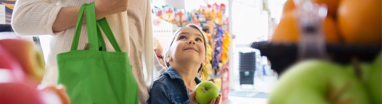 This banner image shows a child holding a green apple in his hand, watching his mother, and smiling.