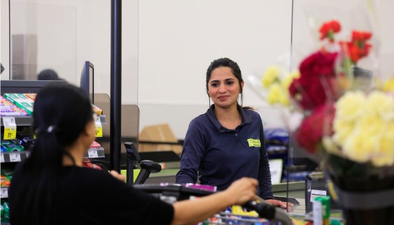 In this image, A cashier in a black shirt attends to a customer at a grocery store checkout.